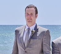 The groom in a tuxedo on the beach.